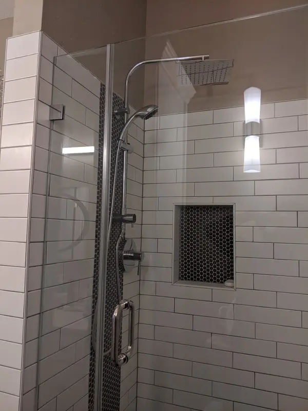 Modern tiled shower installation with white subway tile, glass shower door, built-in niche, rainfall showerhead, handheld sprayer, and clean accent tile details for a stylish bathroom upgrade.